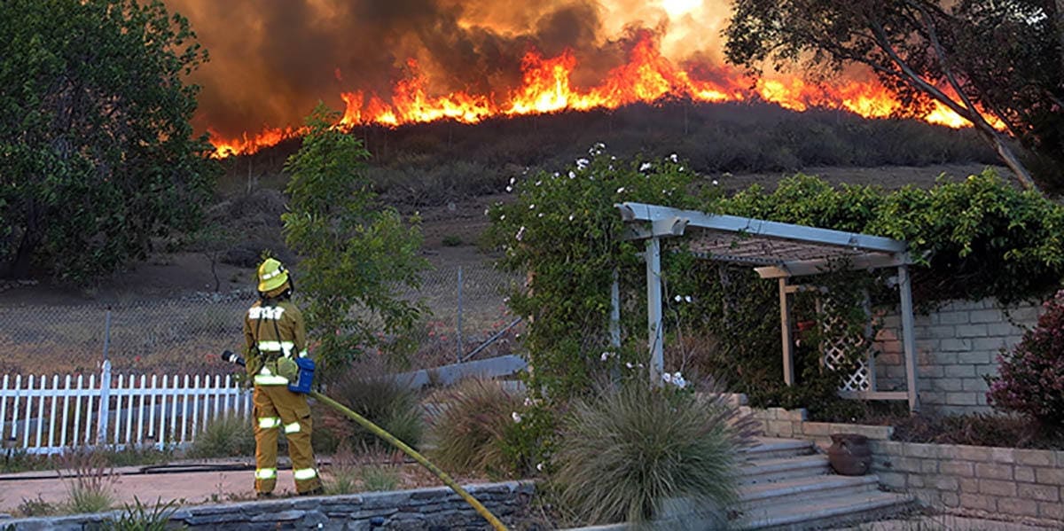 Firefighter spraying water on hillside fire near Triunfo Water & Sanitation District facility.
