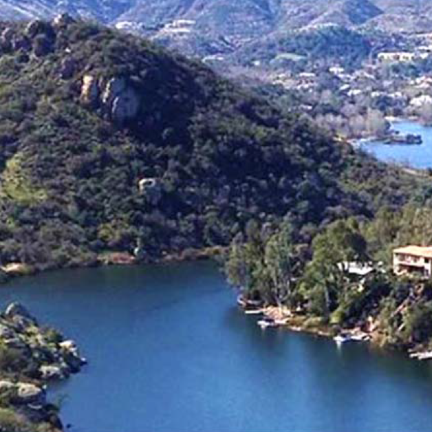 A lush lakeside landscape with hills and residential homes in the background.